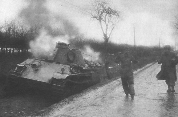 An American soldier escorts a German crewman from his wrecked Panther tank